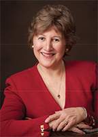 Patricia Gabow has short brown hair. She is wearing a red jacket and has her arms folded in front, hands resting on top of each other.