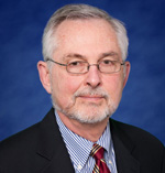 Glenn Steele has white/gray hair, facial hair, and glasses. He is wearing a suit.