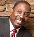Thomas LaVeist has very short black hair and a moustaches. He is wearing a suit and standing in front of a stone wall.