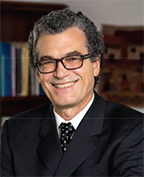 Eliseo Perez-Stable has short curly gray hair and glasses. He is wearing a suit.