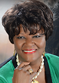 Shirley Marks has short black hair and is wearing a green blouse with a beaded necklace.