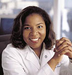 Valerae Lewis has medium-length black hair and is wearing a white coat.