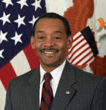 Jonathan Woodson has short black hair and is wearing a suit. He is in front of an American flag.