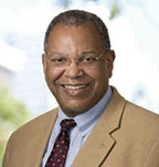 Otis Brawley has very short coily gray hair and glasses. He is wearing a beige suit.