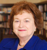 Karen Davis has short brown hair and is wearing a blue jacket. She is in front of some bookshelves.