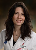 Keila Lopex has long wavy brown hair and is wearing a white coat.