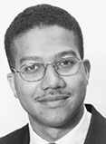 Roderick King has short black hair and glasses. He is wearing a suit.