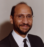 John Lumpkin has short black hair and glasses. He is wearing a suit.
