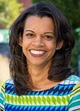 Shairi Turner has medium-length black hair. She is outside and wearing a green and blue patterned blouse.
