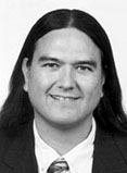 Donald Warne has long straight black hair. He is wearing a suit.