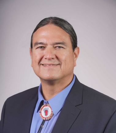 Donald Warne has long straight hair tied back. He is wearing a suit with a bolo tie.