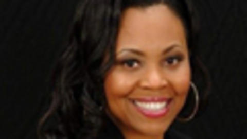 Christina Rosenthal has long black hair. She is wearing a white blouse and black blazer.