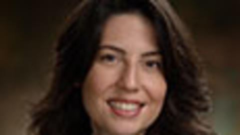 Keila Lopex has long wavy brown hair and is wearing a white coat.