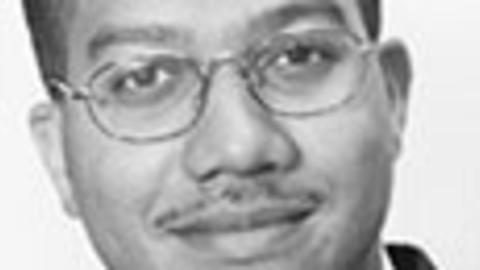 Roderick King has short black hair and glasses. He is wearing a suit.