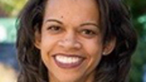 Shairi Turner has medium-length black hair. She is outside and wearing a green and blue patterned blouse.