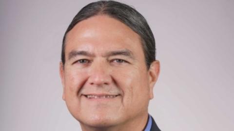 Donald Warne has long straight hair tied back. He is wearing a suit with a bolo tie.