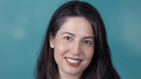 Keila Lopez has long wavy brown hair and is wearing a blue embroidered floral blouse.