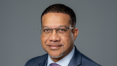 Roderick King has short black hair and frameless glasses. He is wearing a blue suit with a patterned tie and pocket square.
