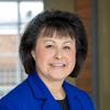 Yvette Roubideaux has short black hair with bangs. She is wearing a blue blazer and black top.