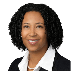 Dora Hughes is wearing a black blazer and white shirt. She has chin-length curly black hair.