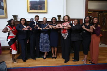 Several fellows and Joan Reede make the Alpha Kappa Alpha and Delta Sigma Theta signs in the Waterhouse Room in Gordon Hall.