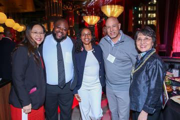Four fellows pose with Ying Wang at Grace By Nia. There are several yellow lights visible above them.