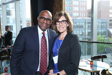 Two alumni fellows stand in front of the large windows at Grace By Nia. 