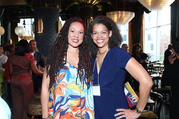 Two alumni fellows pose for a picture as others mingle behind them.