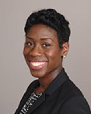 Adjoa Anyane-Yeboa has short black hair. She is wearing a patterned black-and-white blouse and a black blazer.