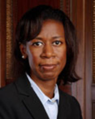 Ashaunta Tumblin has chin-length straight black hair. She is wearing a white shirt and black blazer.
