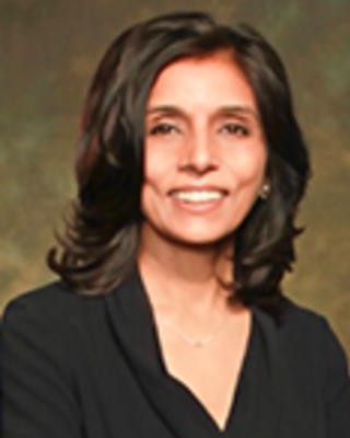 Monica Bharel has medium length black hair and is wearing a black blouse.