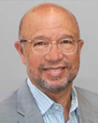 Durado Brooks is a bald man with glasses and light facial hair. He is wearing a striped shirt and light gray blazer.