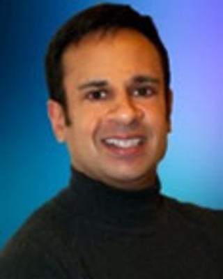 Chandak Ghosh is wearing a black turtleneck. He is in front of a multicolor blue-purple gradient background.