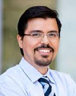 Luis Castellanos has short black hair, a goatee, and moustache. He is wearing glasses.