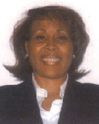 Connie Gistand has chin-length brown hair and is wearing a white shirt with a black blazer.