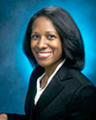 Nicole DelCastillo has shoulder-length black hair. She is wearing a white blouse and black blazer.