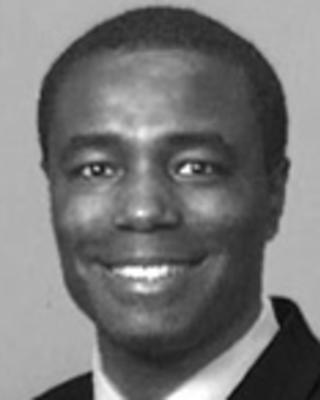 Kansky Delisma has cropped black hair and is wearing a suit.
