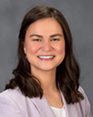 Diana Rubio has medium-length brown hair. She is wearing a white shirt and light purple blazer.
