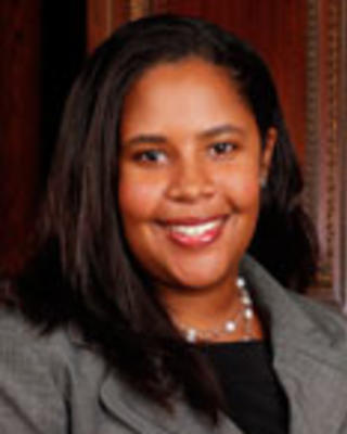 Dustyn Baker has medium straight black hair. She is wearing a black shirt, gray blazer, and necklace.