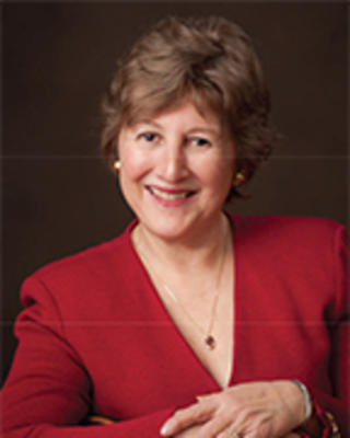 Patricia Gabow has short brown hair. She is wearing a red jacket and has her arms folded in front, hands resting on top of each other.