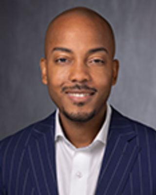 Darrell Gray is a bald man with light facial hair. He is wearing a white shirt and striped blue blazer.