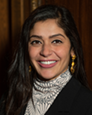 Nasrien Ibrahim has long black hair. She is wearing a printed turtleneck and black blazer.