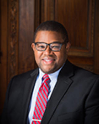 Ross Jones has short black hair and is wearing a suit.