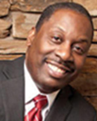 Thomas LaVeist has very short black hair and a moustaches. He is wearing a suit and standing in front of a stone wall.