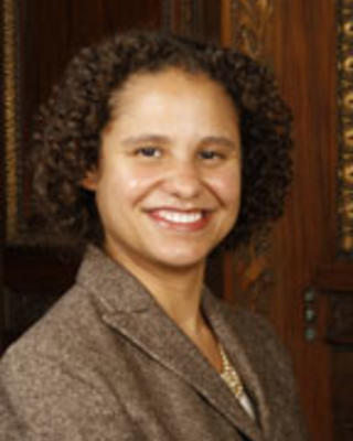 Julea McGhee has short curly brown hair and is wearing a brown blazer.
