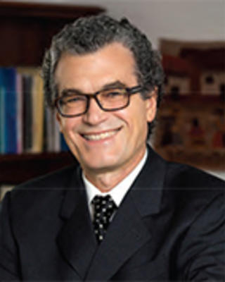 Eliseo Perez-Stable has short curly gray hair and glasses. He is wearing a suit.