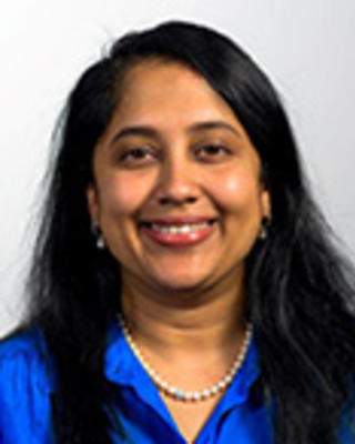 Preeta Chidambaran has long straight black hair and is wearing a blue shirt with a pearl necklace.