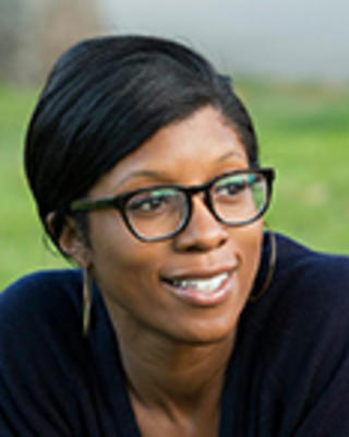 Rhea Boyd has short black hair and glasses. She is outside and looking to the side.