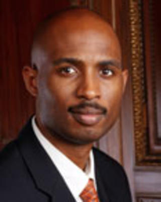 Roy Wade is a bald man with a moustashe. He is wearing a suit.