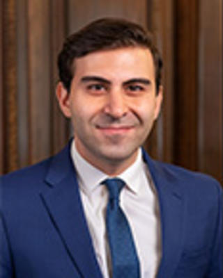 Hussein Saghir has short brown hair. He is wearing a blue suit.